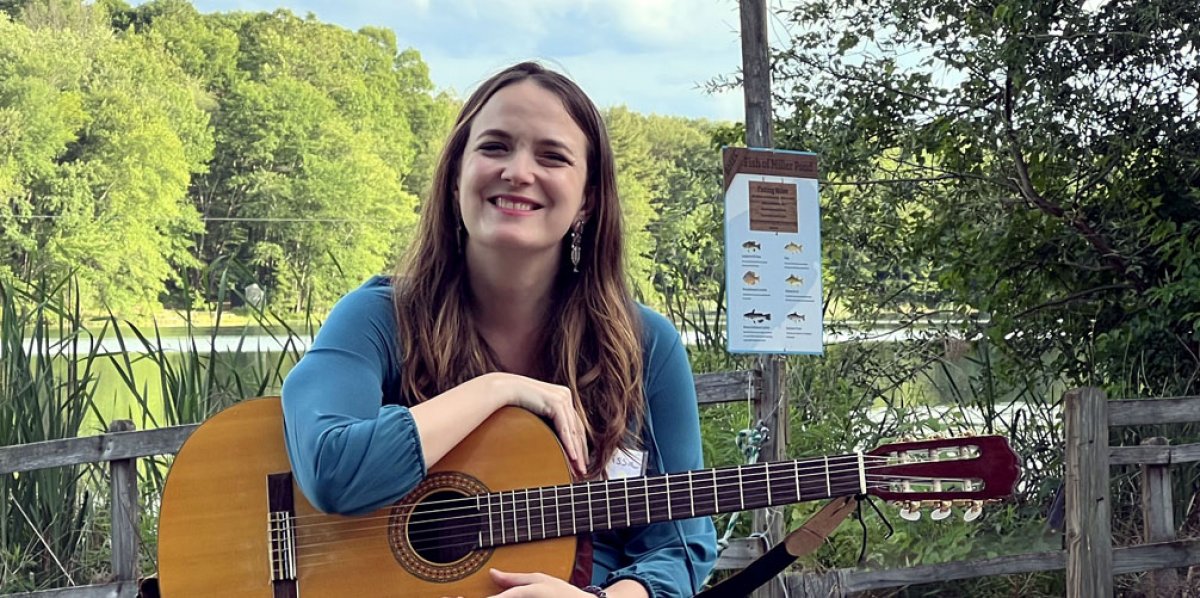 Cantor Melissa Berman sitting outdoors holding guitar